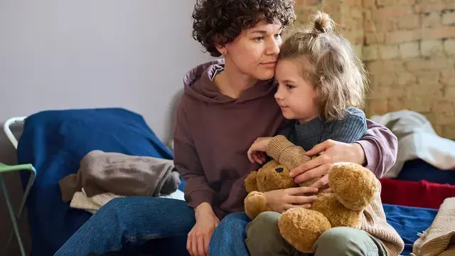 Mother comforting daughter who is holding her teddy bear toy